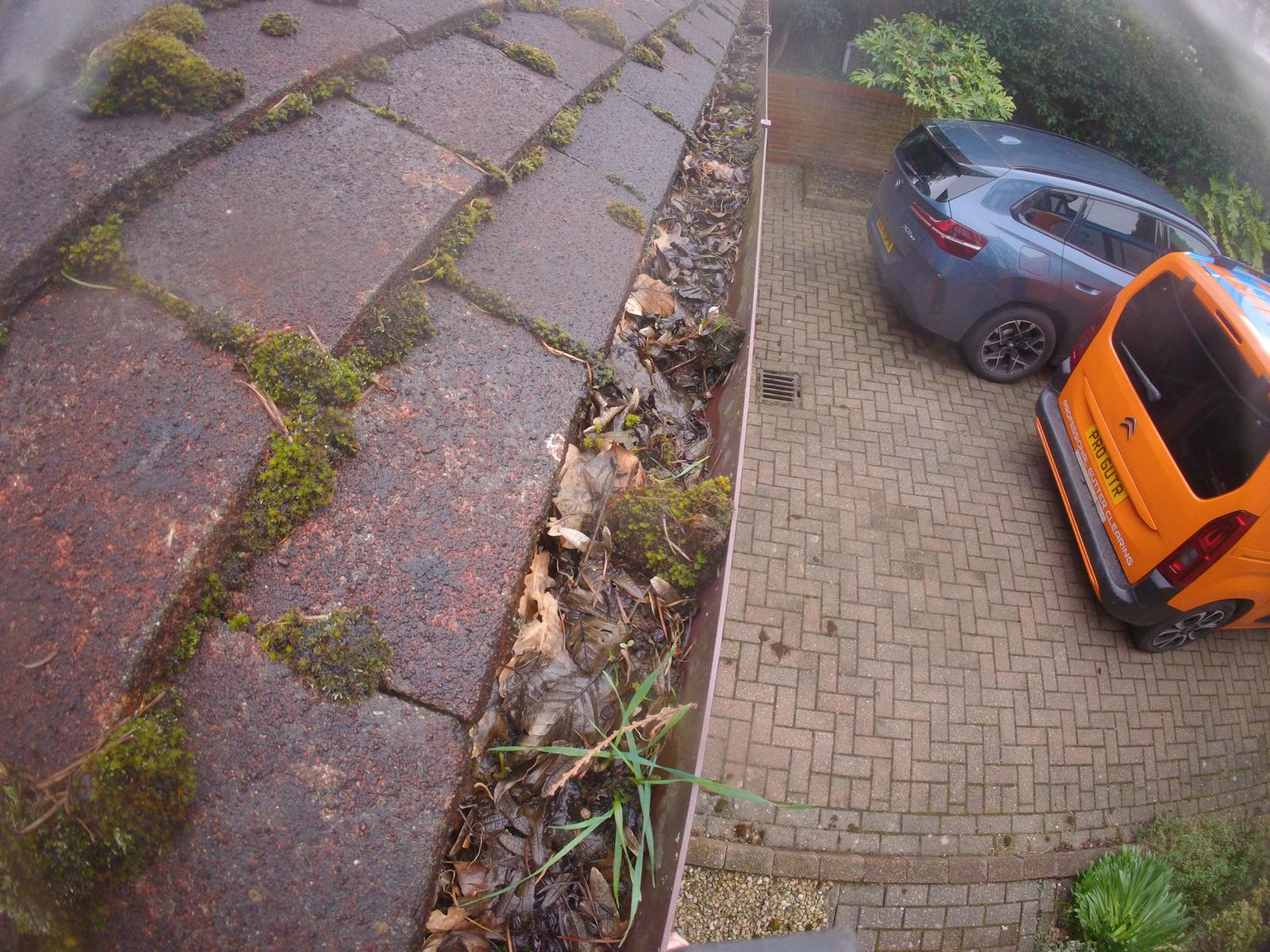 Gutter clogged with debris and leaves requiring professional clearing, Gutter Pro van visible below