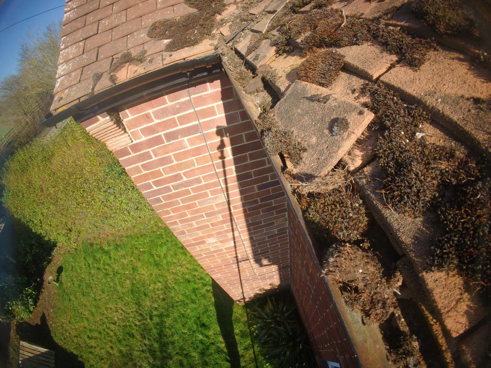 Mossy roof tiles and blocked gutter channel at corner of residential property